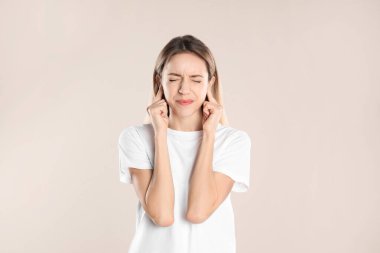 Bej arka planda parmaklarıyla kulaklarını kapatan duygusal genç bir kadın.