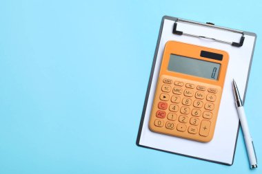 Hesap makinesi, pano ve kalem açık mavi arka planda, düz yerde. Metin için boşluk