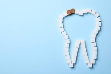 Diş anahatlarında beyaz olanlar arasında iki esmer şeker küpü. Caries 'i sembolize ediyor, düz yatıyordu. Tehlikeli tatlılar.