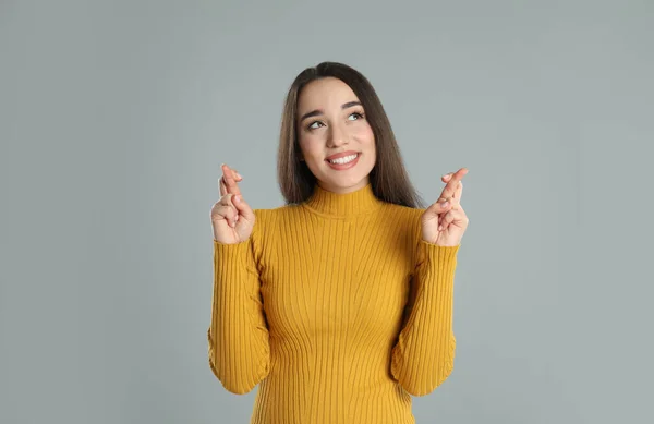 Mujer Joven Emocionada Sosteniendo Los Dedos Cruzados Sobre Fondo Gris —  Fotos de Stock