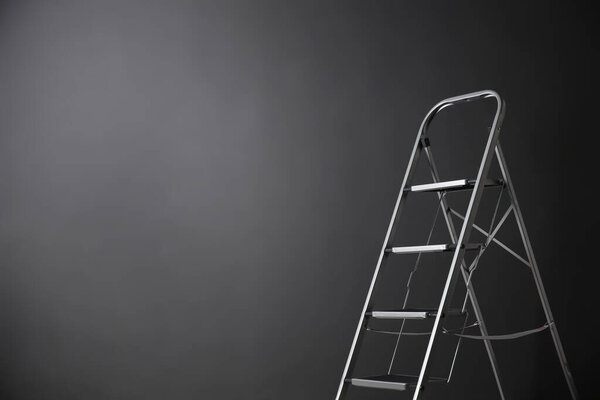 Modern metal stepladder against grey background. Space for text