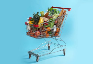 Alış veriş arabası açık mavi arka planda yiyeceklerle dolu.
