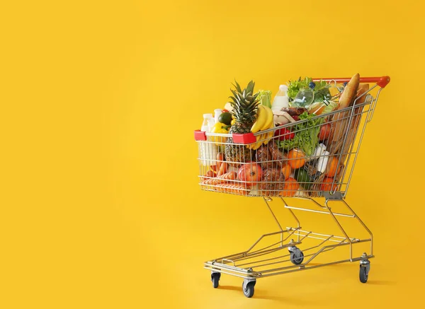 Shopping cart full of groceries on yellow background. Space for text