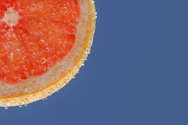 Slice of grapefruit in sparkling water on blue background, closeup with space for text. Citrus soda