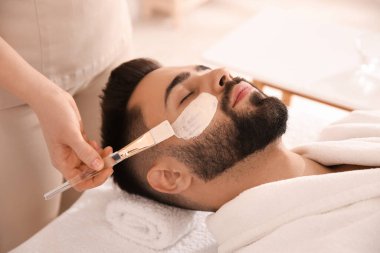 Kozmetik uzmanı spa salonunda adamın yüzüne maske takıyor.