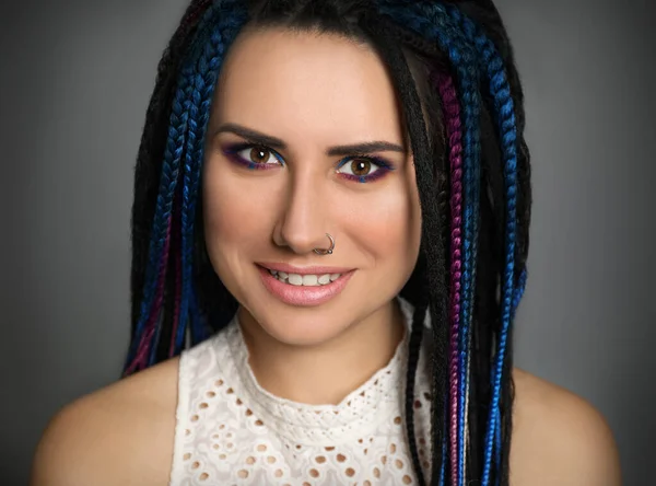 Beautiful young woman with nose piercing and dreadlocks on grey background