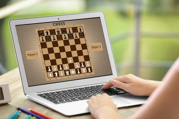 Woman playing online chess on laptop at table, closeup