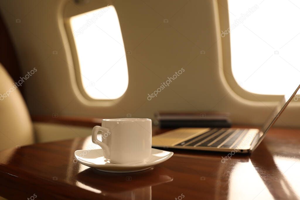 Cup of coffee with laptop and notebooks on table in airplane