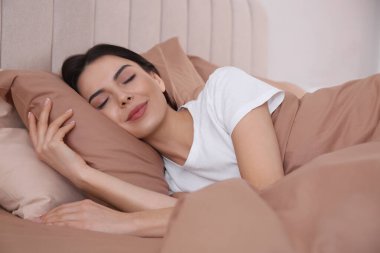 Bej çarşaflarla rahat bir yatakta uyuyan kadın.