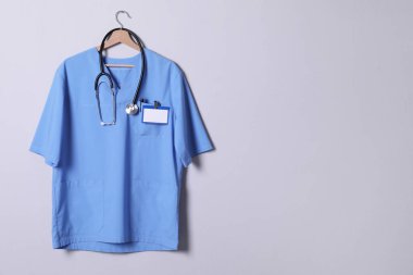Doktor gömleği steteskop, rozet ve açık gri arka planda asılı kalem. Metin için boşluk