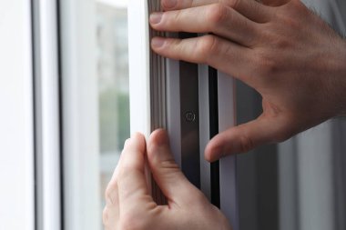İşçi pencereye plastik cereyan bandı yerleştiriyor, yakın plan.