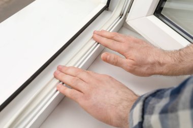 İşçi pencereye plastik cereyan bandı yerleştiriyor, yakın plan.