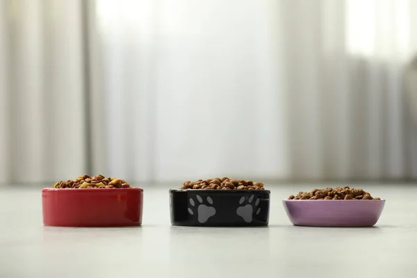 Dry food in pet bowls on floor indoors, space for text
