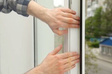 İşçi pencereye plastik cereyan bandı yerleştiriyor, yakın plan.
