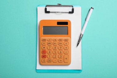 Açık mavi zemin üzerinde hesap makinesi, pano ve kalem, düz yatar