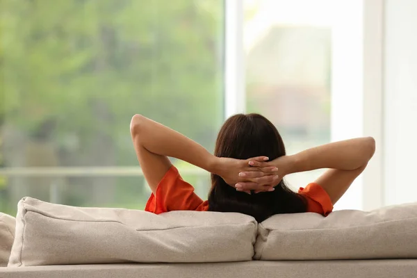 Young woman relaxing on sofa at home, back view