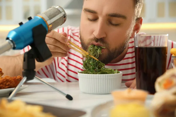 Food blogger eating near microphone at table in kitchen, closeup. Mukbang vlog