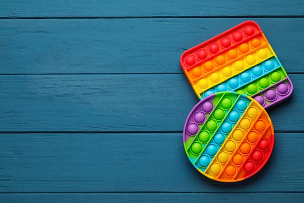 Rainbow pop it fidget toys on blue wooden table, flat lay. Space for text