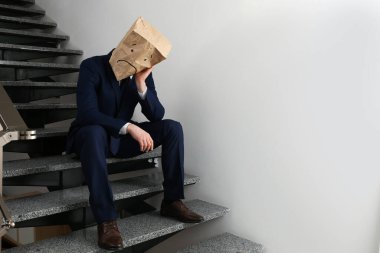 Kapalı mekanda üzgün yüzü çizilmiş kağıt poşet giyen bir adam. Metin için boşluk