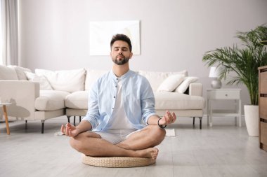 Genç adam evdeki saman yastığında meditasyon yapıyor.