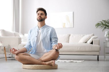 Genç adam evde saman yastığı üzerinde meditasyon yapıyor, mesaj için yer var.