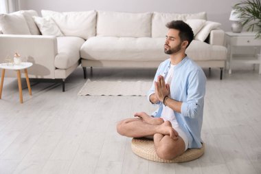 Genç adam evde saman yastığı üzerinde meditasyon yapıyor, mesaj için yer var.