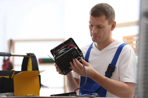 Professional technician repairing electric fan heater with screwdriver at table indoors