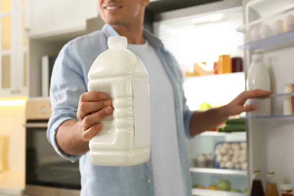 Man with gallon of milk near refrigerator in kitchen, closeup