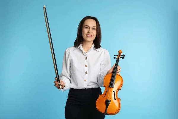 Music teacher with violin and bow on turquoise background