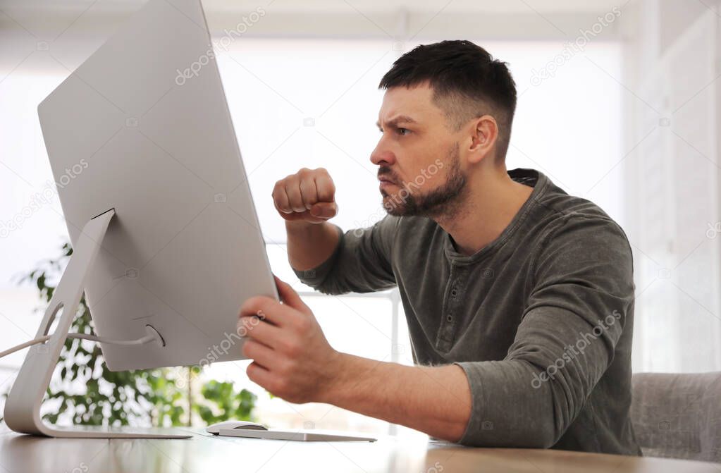 Emotional man in front of computer at workplace. Online hate concept