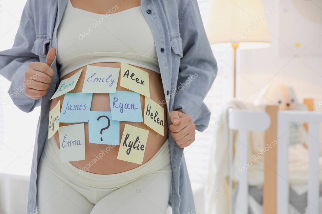 Pregnant woman with different baby names on belly at home, closeup. Space for text