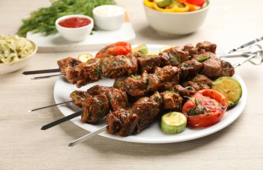 Metal skewers with delicious meat and vegetables served on white wooden table clipart