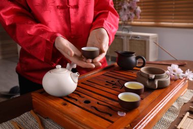 Master offering cup of freshly brewed tea during traditional ceremony at table, closeup clipart