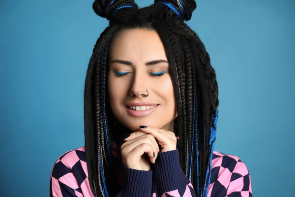 Beautiful young woman with nose piercing and dreadlocks on light blue background