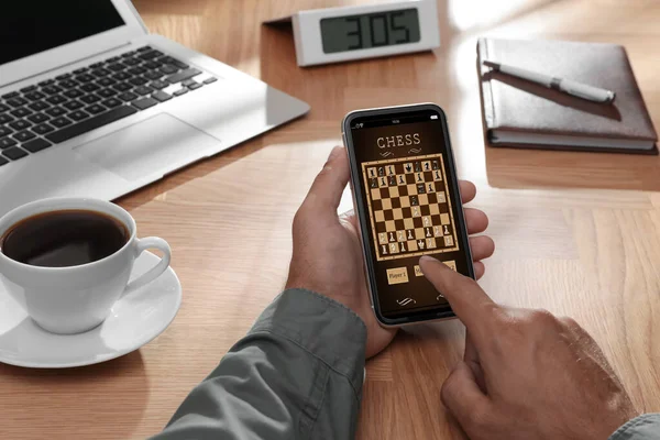 Man playing online chess on smartphone at table, closeup