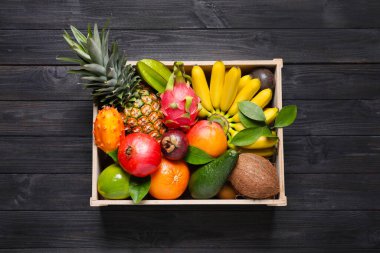 Siyah ahşap masanın üstünde değişik egzotik meyveler olan sandık.