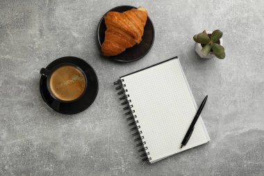 Not defteri, bir fincan aromatik kahve, lezzetli kruvasan ve gri masanın üzerine serilmiş bitki.