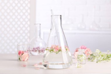 Beyaz ahşap masanın üzerinde gül çiçekleri olan matara. Gerekli yağ çıkarma