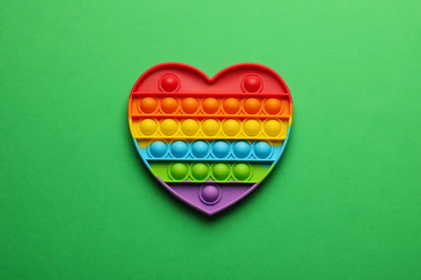 ハート型の虹ポップそれフィジェットおもちゃで緑の背景 トップビュー — ストック写真