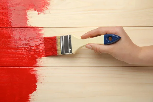 Woman painting wooden surface with red dye, top view