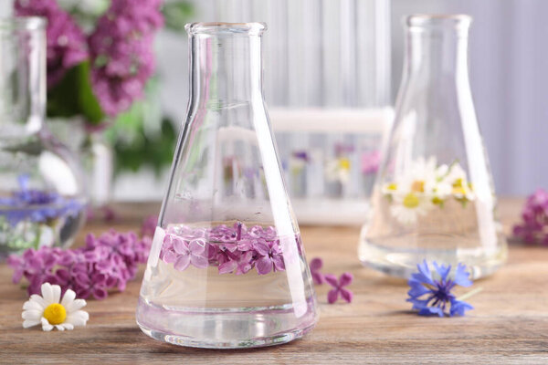 Flask with lilac flowers on wooden table, space for text. Essential oil extraction