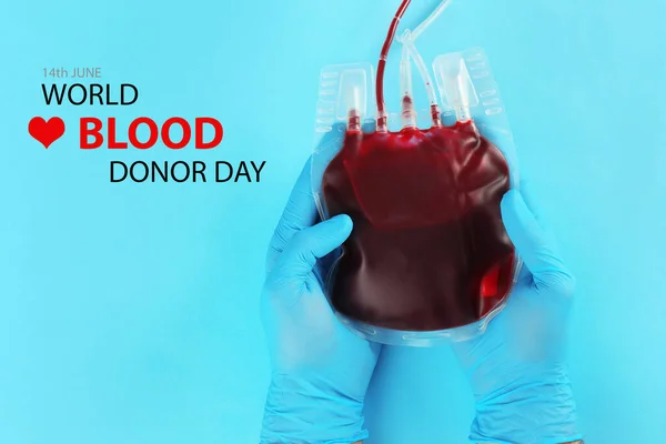 World Donor Day. Doctor in gloves holding blood pack on light blue background, top view