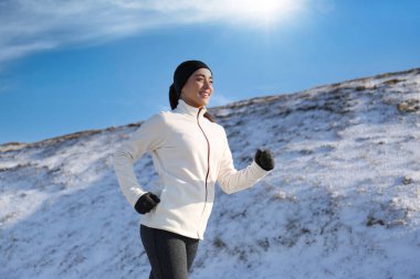 Kışın karlı tepenin yanından koşan mutlu kadın. Açık hava spor egzersizleri.
