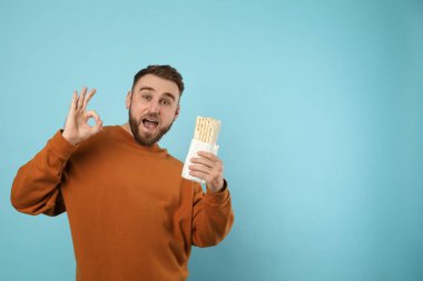 Heyecanlı genç adam lezzetli bir shawarma ile turkuaz arka plan, mesaj için yer