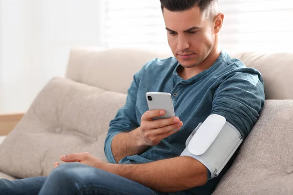 남자는 집안에서 혈압을 현대식 모니터와 스마트폰으로 검사한다 — 스톡 사진