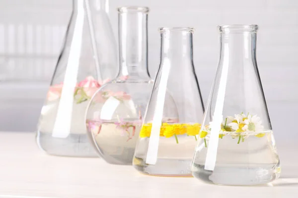 Szkło Laboratoryjne Różnymi Kwiatami Białym Drewnianym Stole Niezbędna Ekstrakcja Oleju — Zdjęcie stockowe