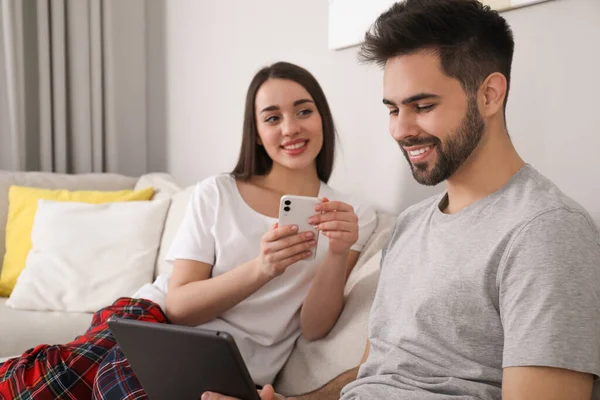 Casal Feliz Pijama Com Gadgets Sofá Casa — Fotografia de Stock