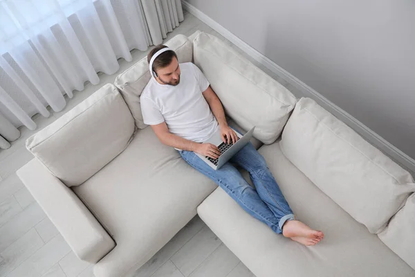 Mann Mit Laptop Und Kopfhörer Sitzt Hause Auf Sofa — Stockfoto