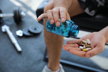 Sportsman with bottle of pills in gym, closeup. Doping concept clipart