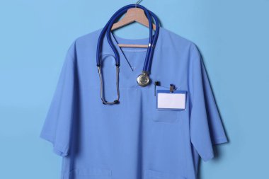 Doktor gömleği steteskop, rozet ve kalem açık mavi arka planda asılı.